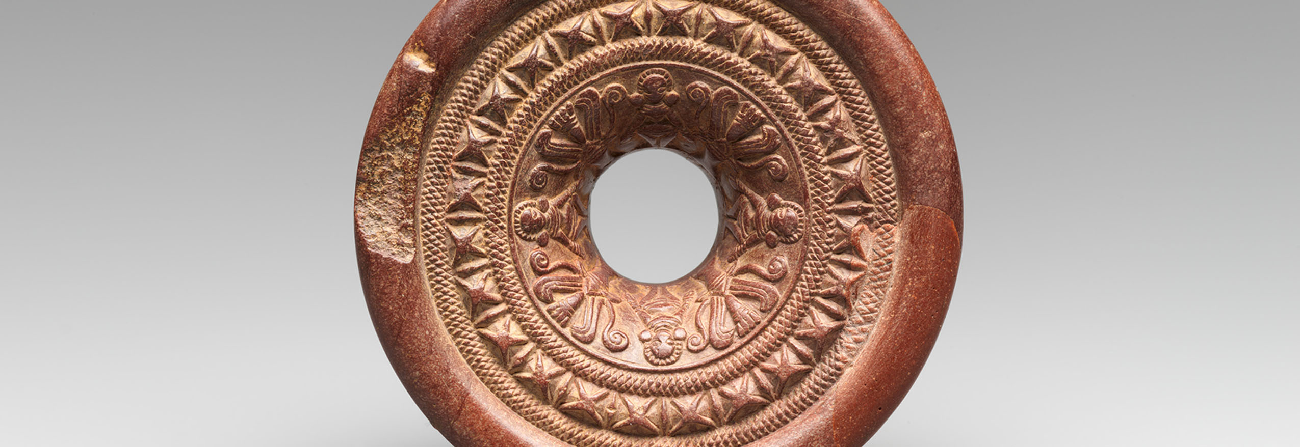 A stone ring with bands of designs depicting female deities, plants and geometric patterns.