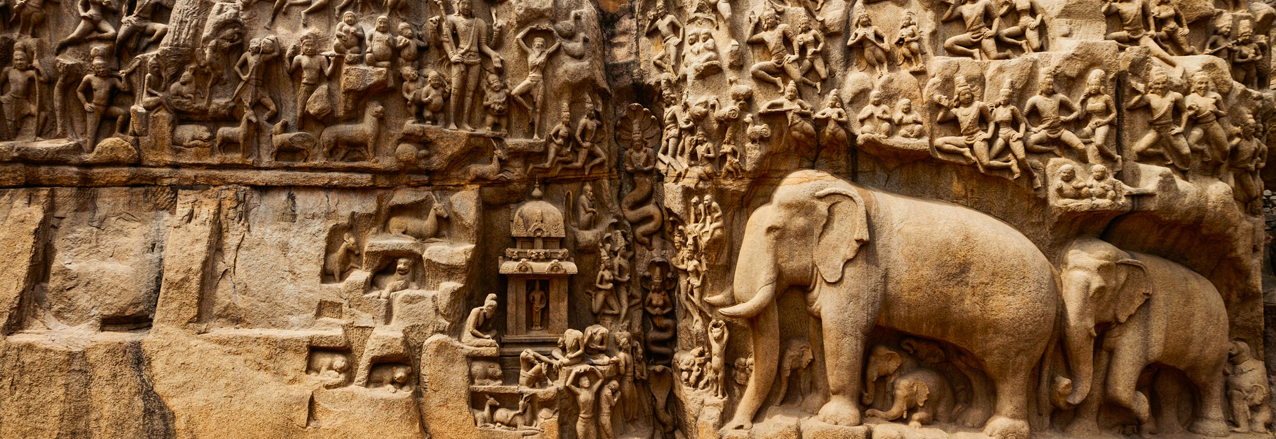 A rock-cut relief of a Hindu mythological scene with carved figures of elephants, deities and other divine beings.