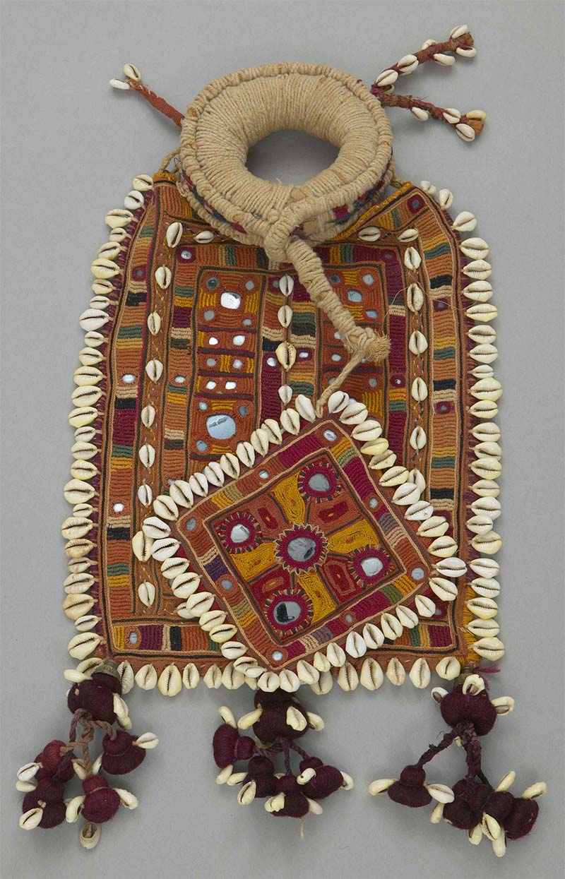 A vividly coloured handwoven head ring, with Banjara embroidery and mirror-work across it, cowry shells decorating its edges, and tassels at its bottom.