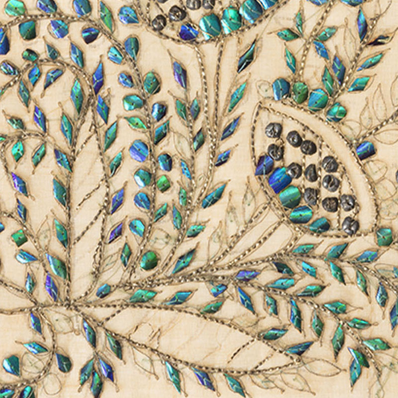 A detail of textile with leaf-shaped beetle wings embellishing an embroidered plant.