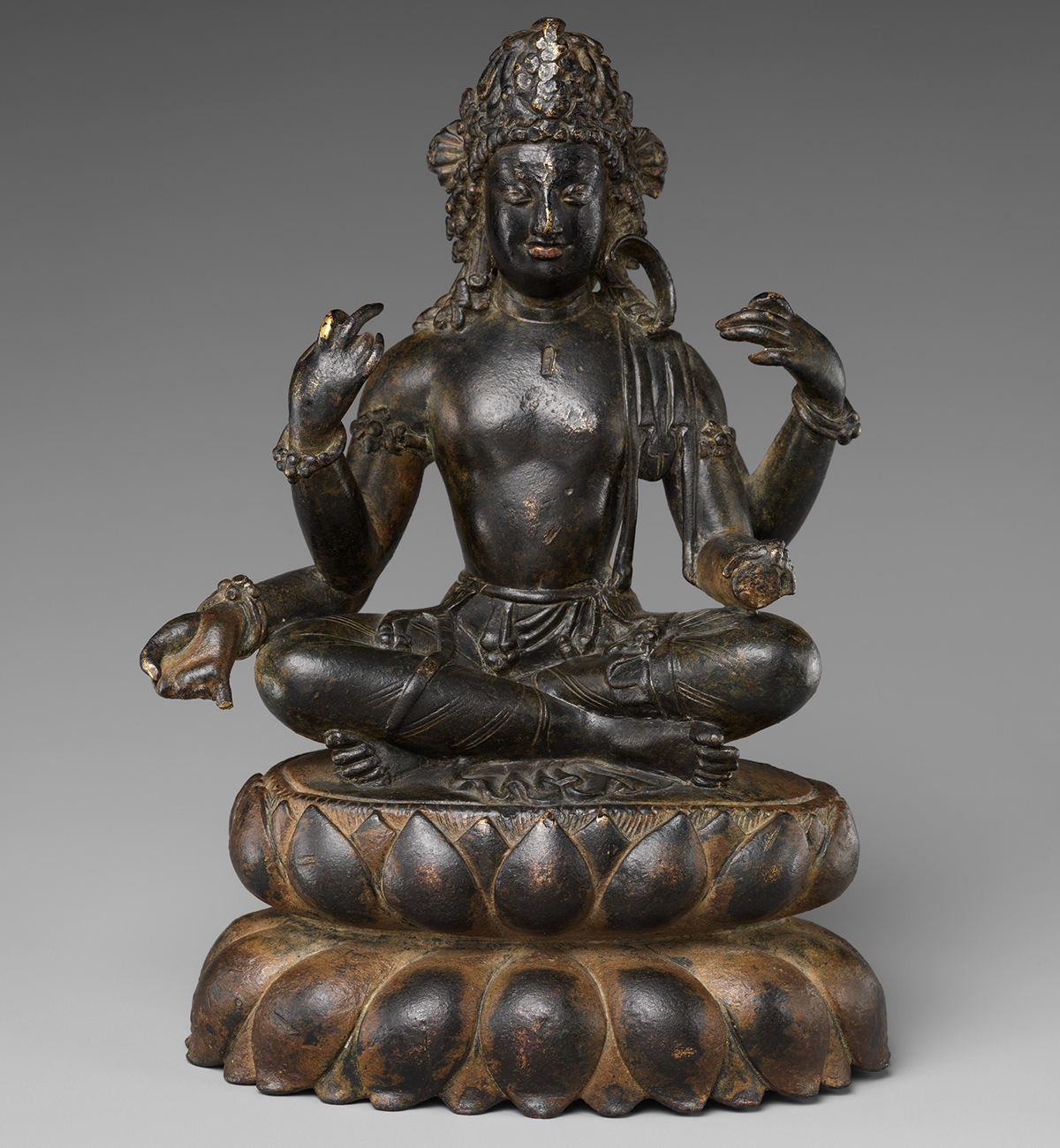 A brass statue depicting the Bodhisattva Avalokiteshvara seated cross-legged on a lotus.