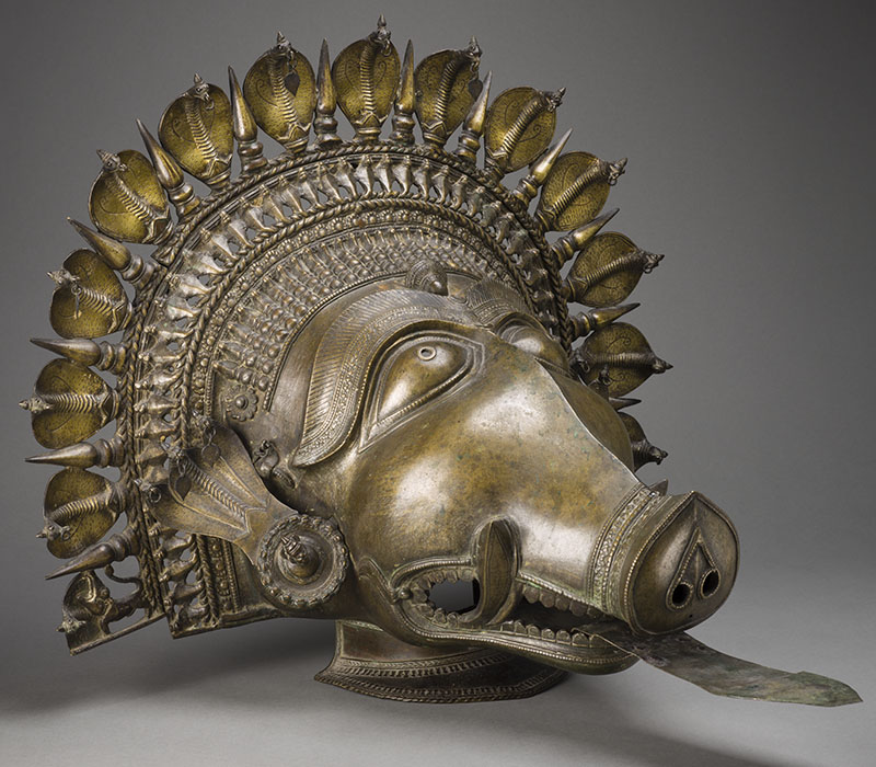 A metal Bhuta mask with the image of a boar, with a protruding tongue, surrounded by smaller images of serpents.