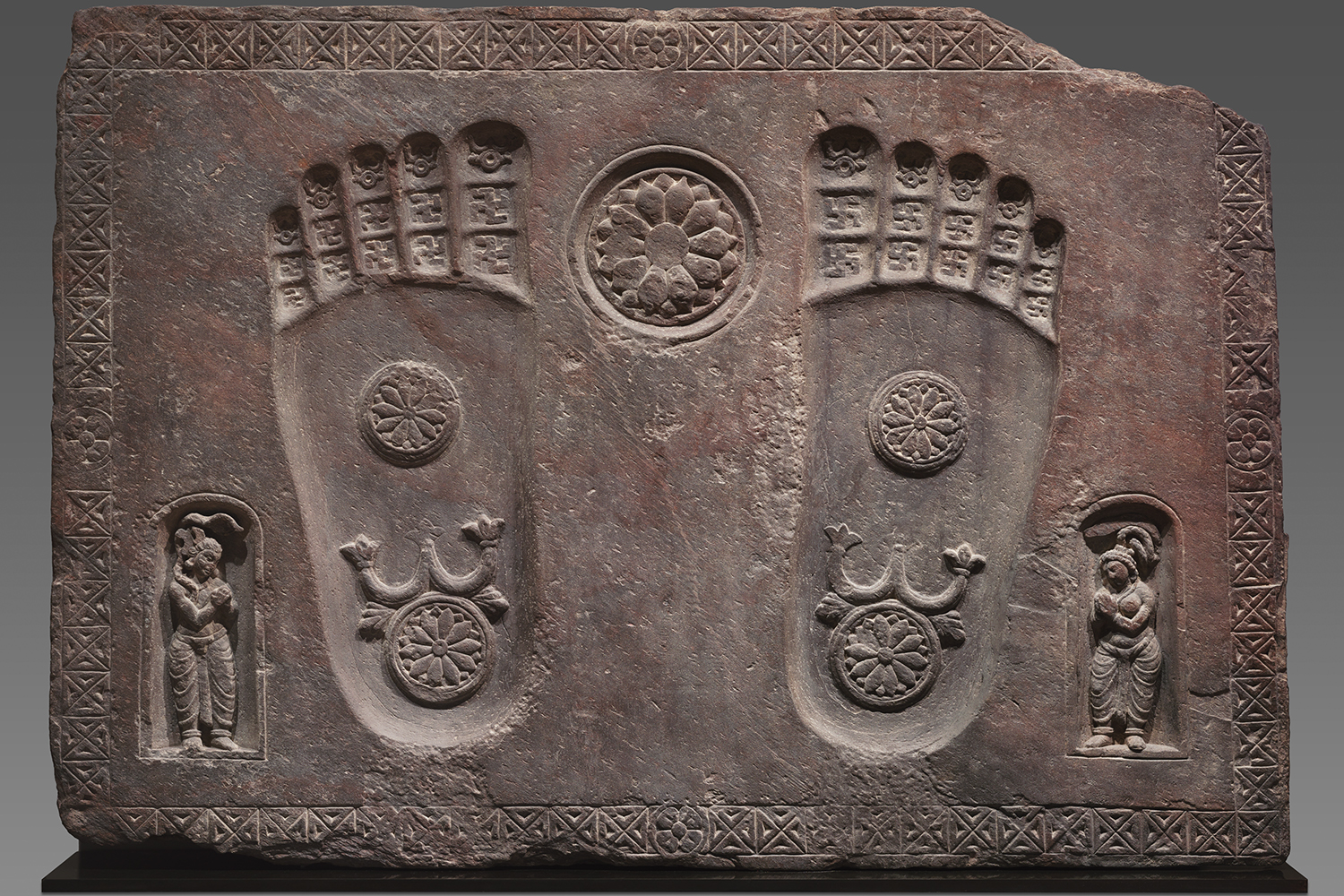 A schist block depicting two footprints with lotuses engraved on them, accompanied by two figures.