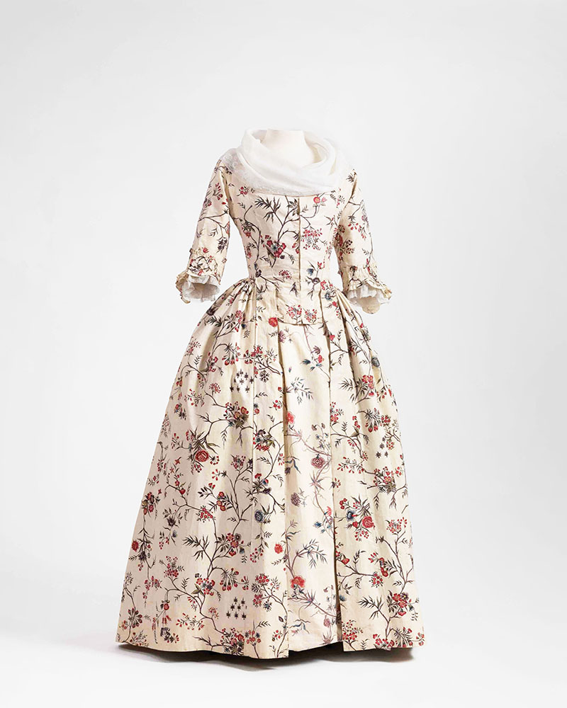 A full-skirted Chintz dress with a cream textile covered in vegetal and floral patterns.