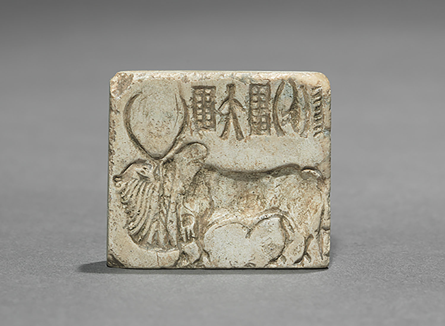 A steatite seal depicting a bull with two horns in the centre and an Indus inscription on the top.