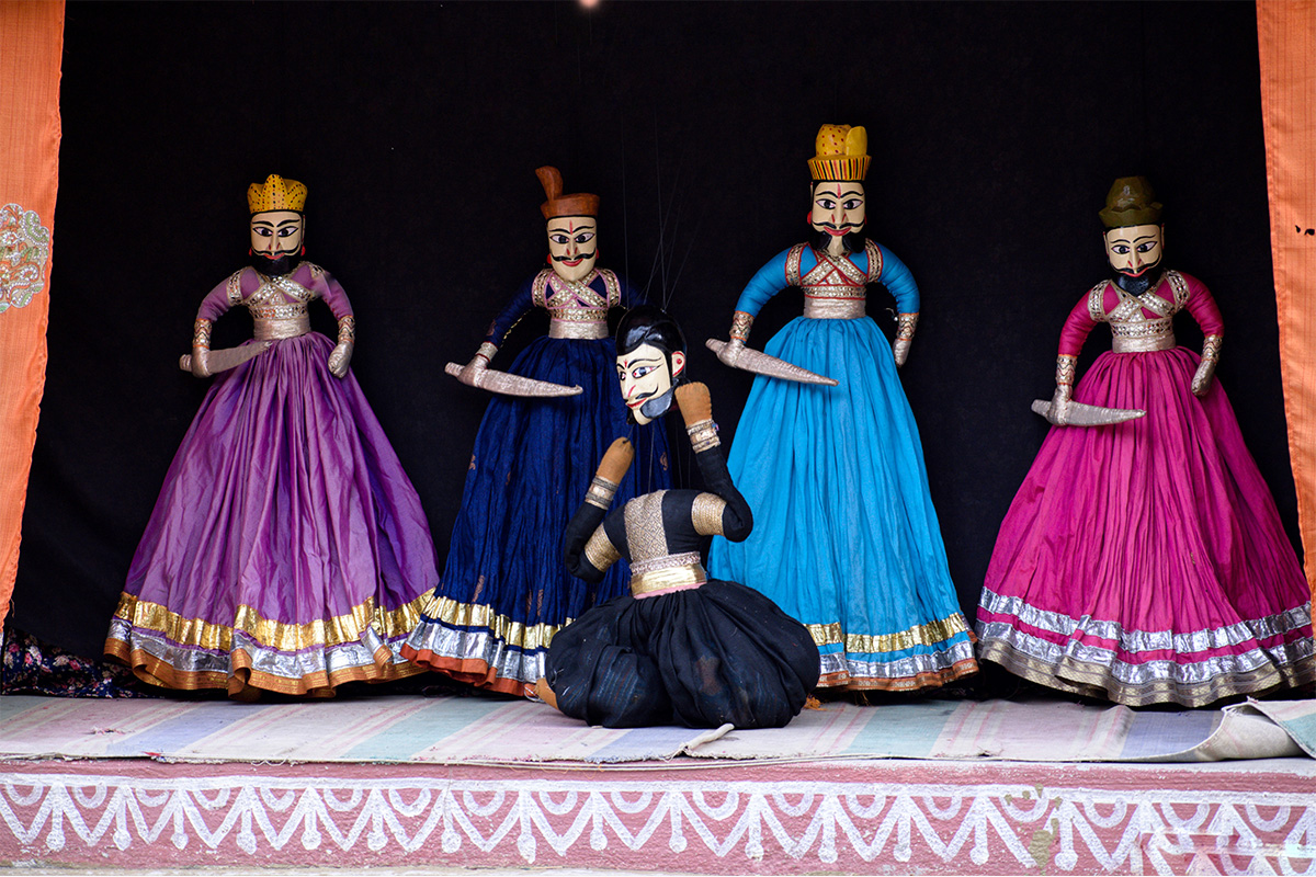 Five Rajasthani string puppets, depicting male characters, on a stage with a black background.