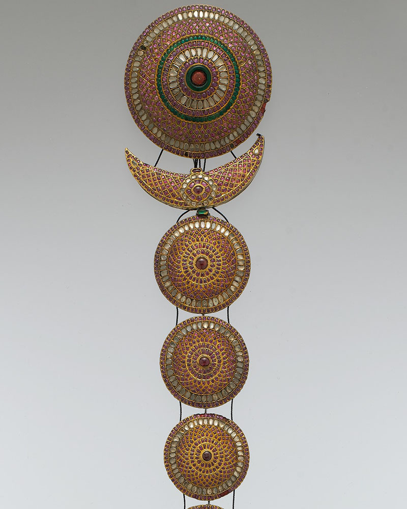 A hair ornament worn over a plait, comprising a crescent and several bejewelled discs, arranged from largest to smallest.