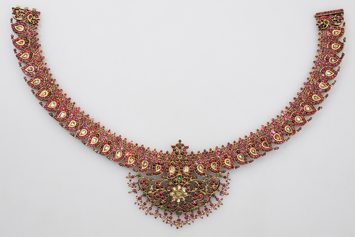 An unfastened necklace made of gold and gems, featuring paisley-shaped units and a floral motif at the centre.