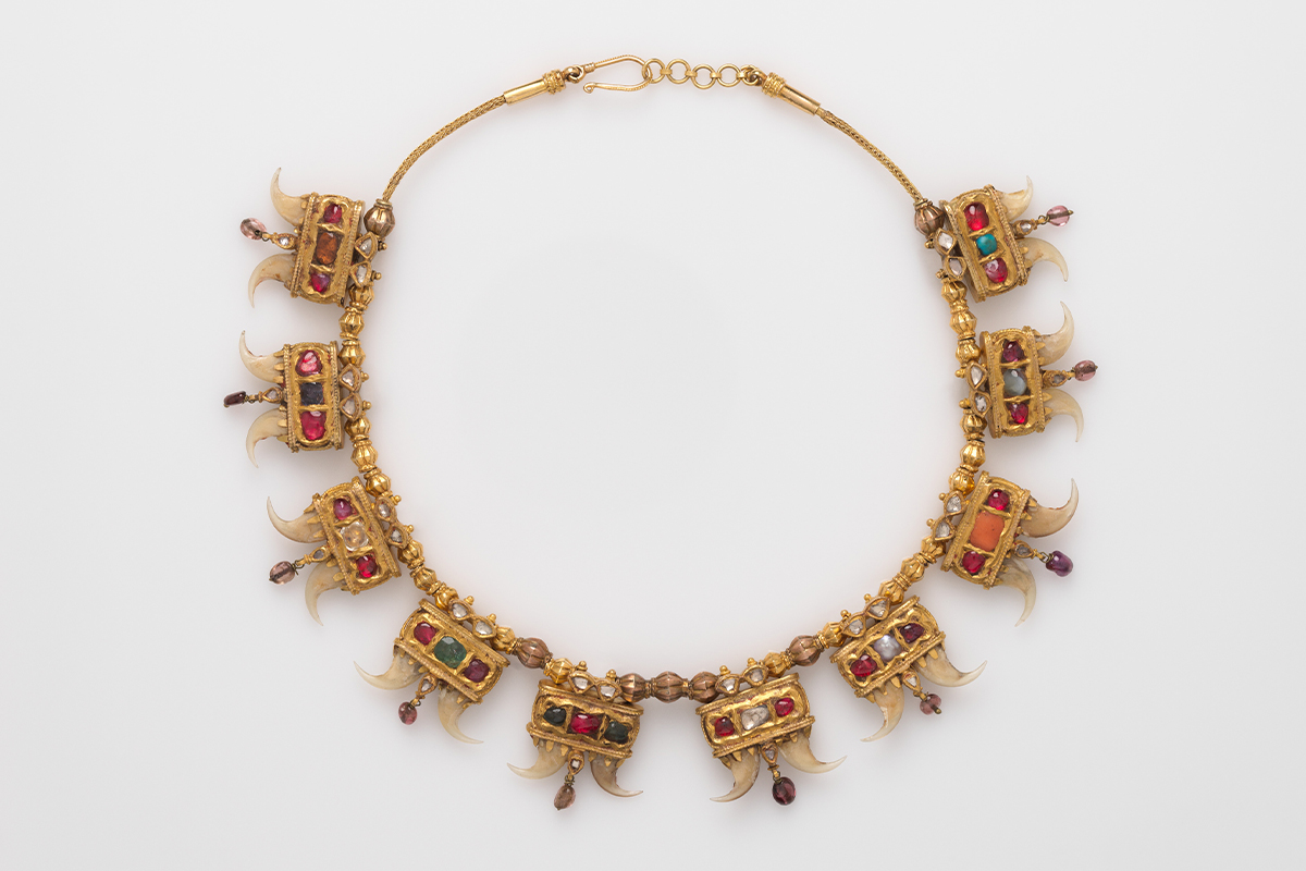 A gold necklace comprising ten units, each featuring gemstones set in kundan and two tiger claws.