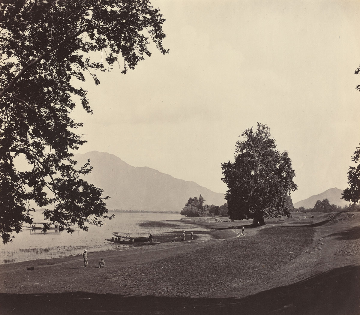 A sepia-toned lakeside view from Kashmir, with some trees in sight and mountain peaks in the distant background.