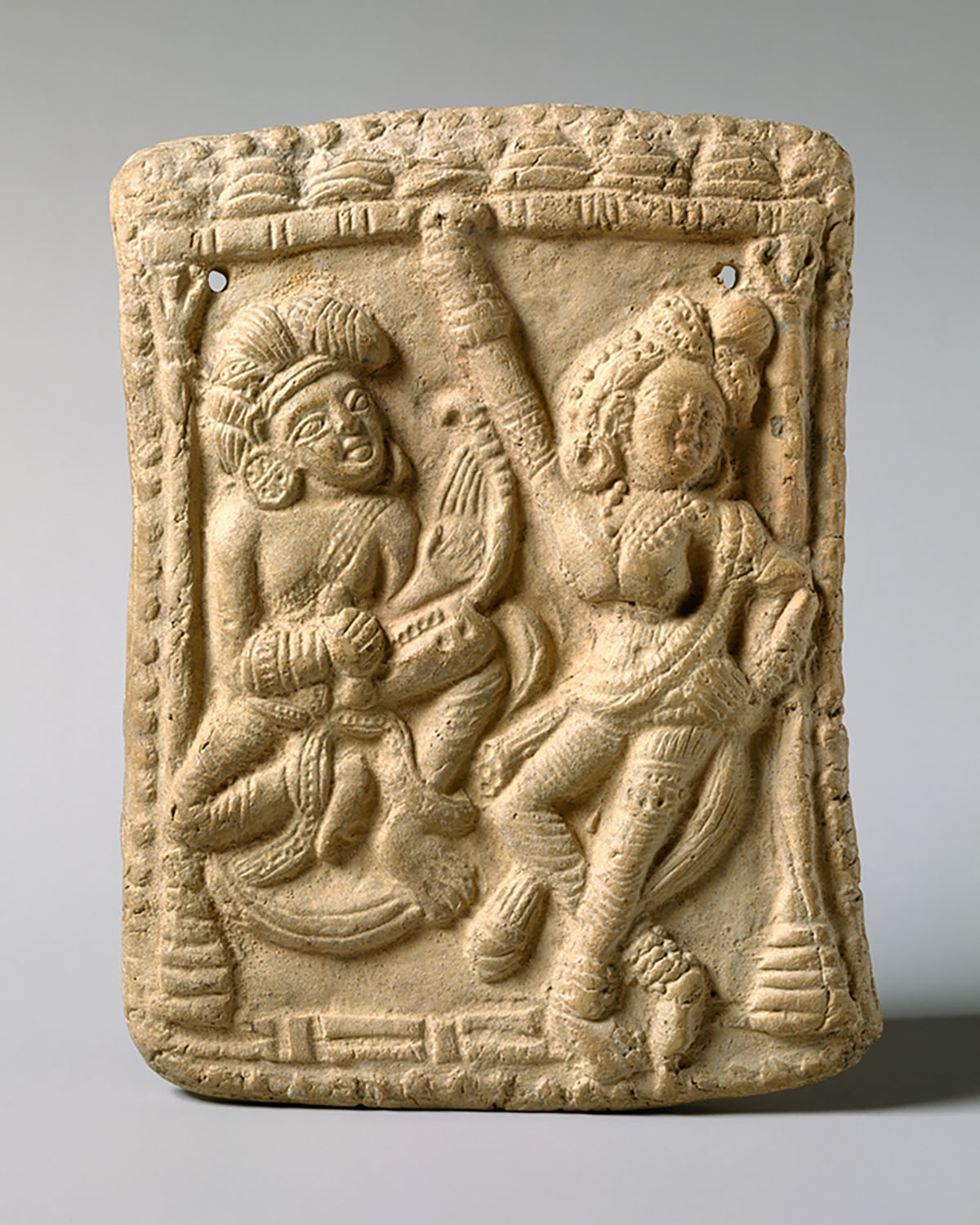 A terracotta plaque depicting a dancing woman on the right and a veena player on the left.