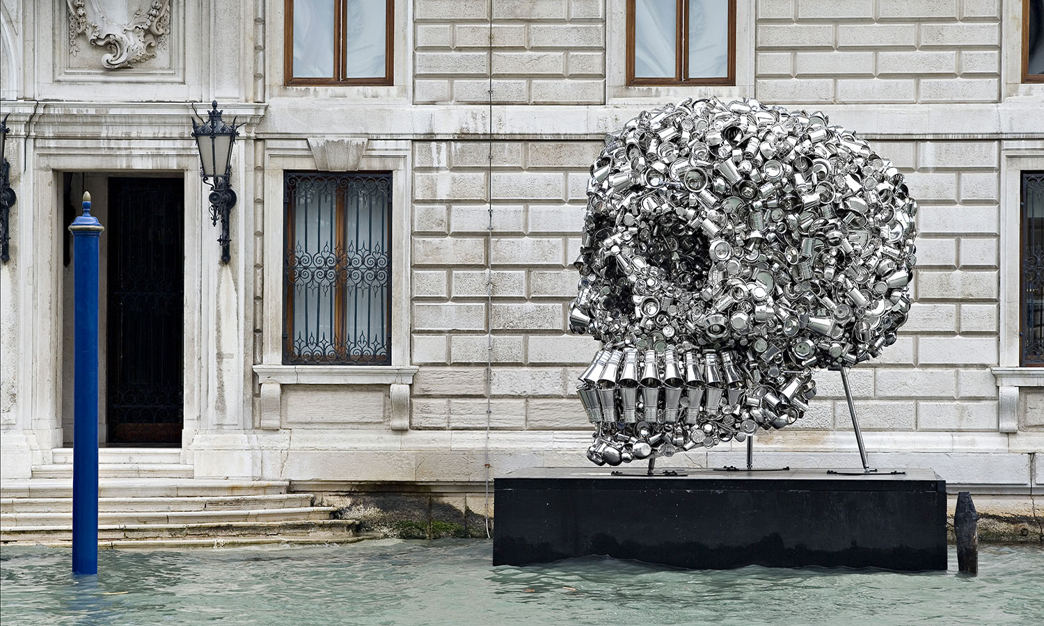 A monumental stainless-steel sculpture of an upturned bucket pouring out kitchen utensils such as plates, glasses and bowls