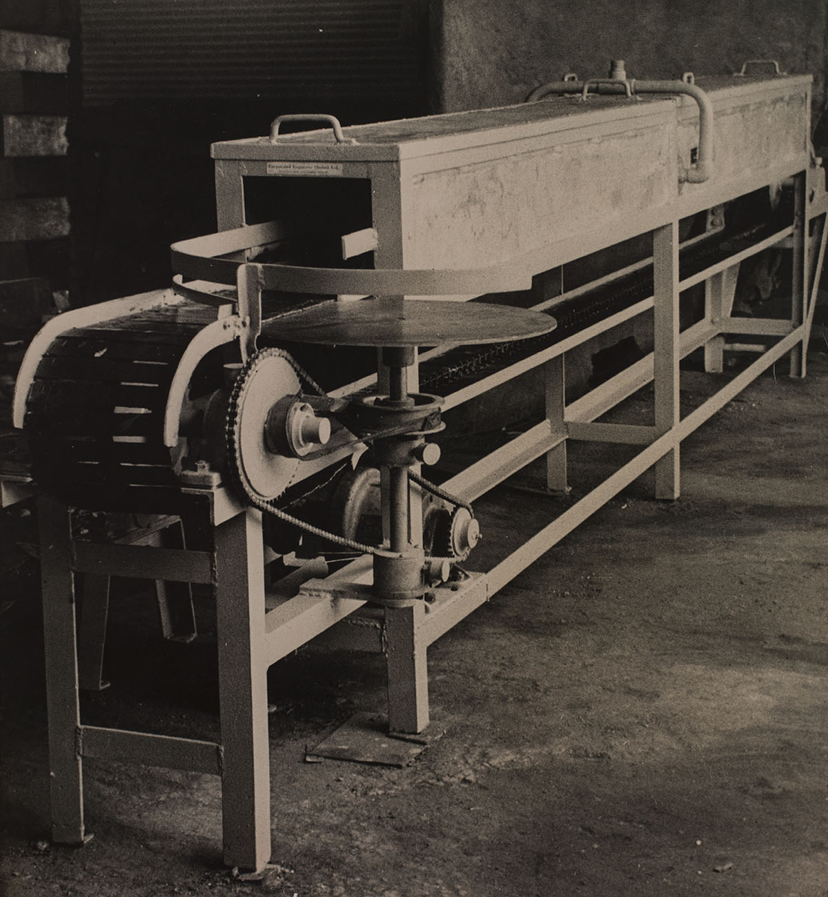 A sepia-toned photograph of an industrial cutting machine inside a factory.