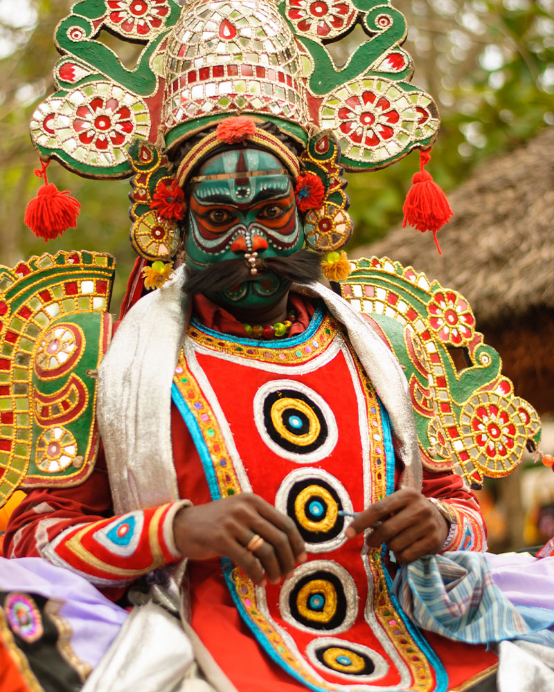 A Therukoothu performer in costume, including a head-dress, large epaulettes, and elaborate facial make-up.