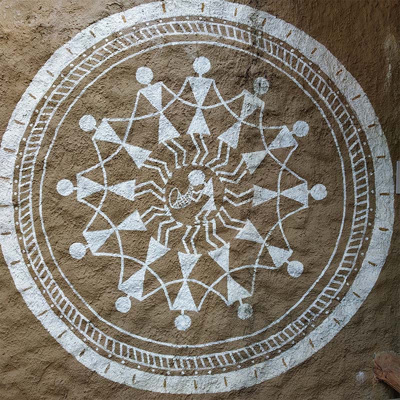 A Warli painting depicting human figures dancing in a circle around the tarpa player.