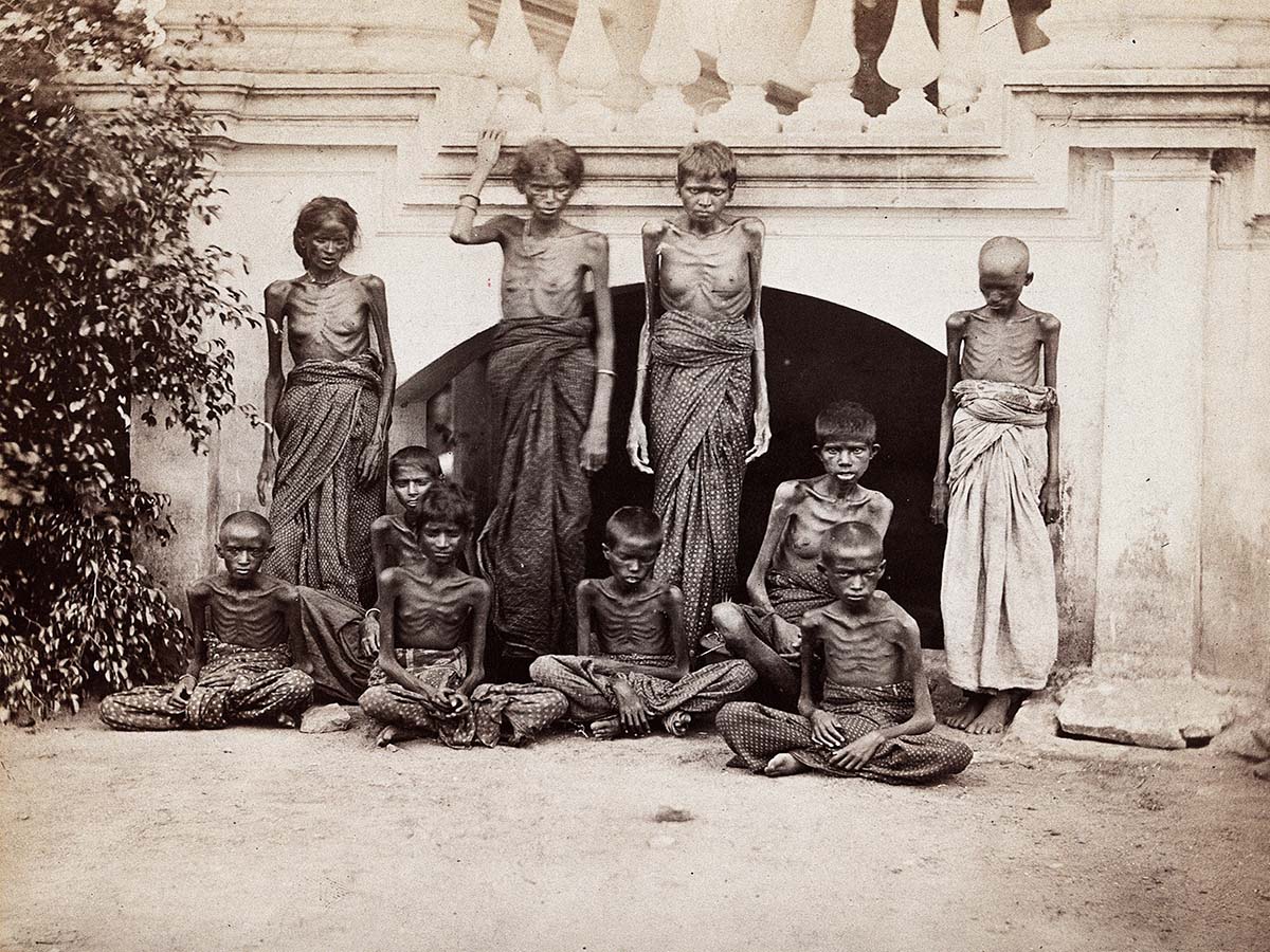 A sepia-toned group photograph of skeletal women and children struck by the Madras famine of 1876–78.