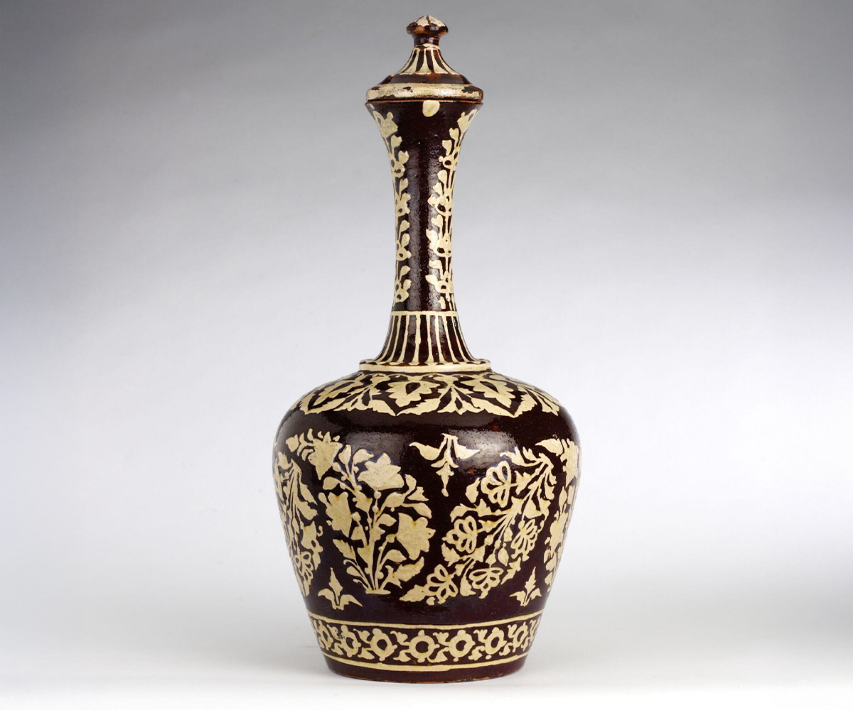 Photograpgh of 19th-century glazed ceramic water bottle with off-white floral designs on a reddish background