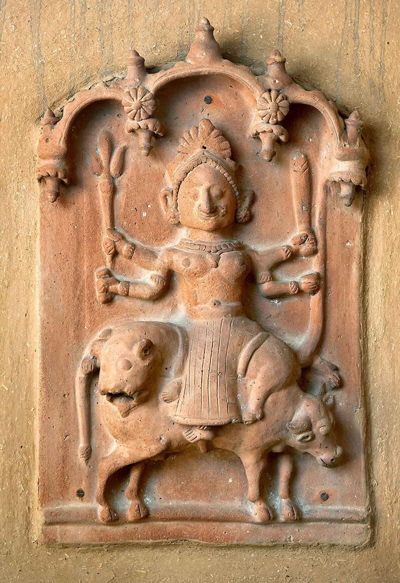 Photograph of a votive plaque of four-armed Keradevi riding a tiger killing the buffalo-headed demon Mahishasur made out of clay, sand dust and donkey dung